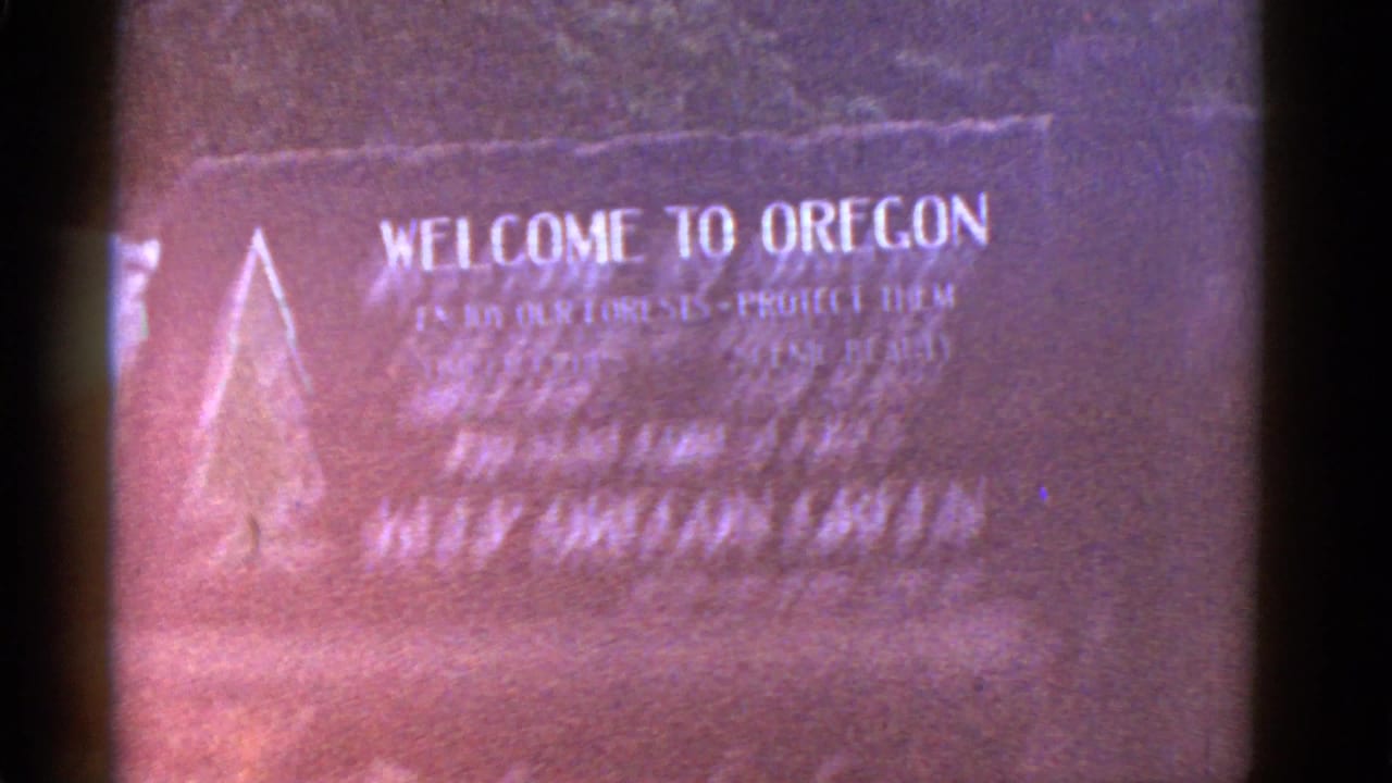Close 8mm frame of a Welcome to Oregon sign, likely from a mid-century travel reel, with soft focus and reddish color fading.