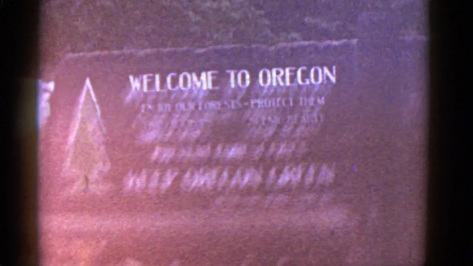 Close 8mm frame of a Welcome to Oregon sign, likely from a mid-century travel reel, with soft focus and reddish color fading.
