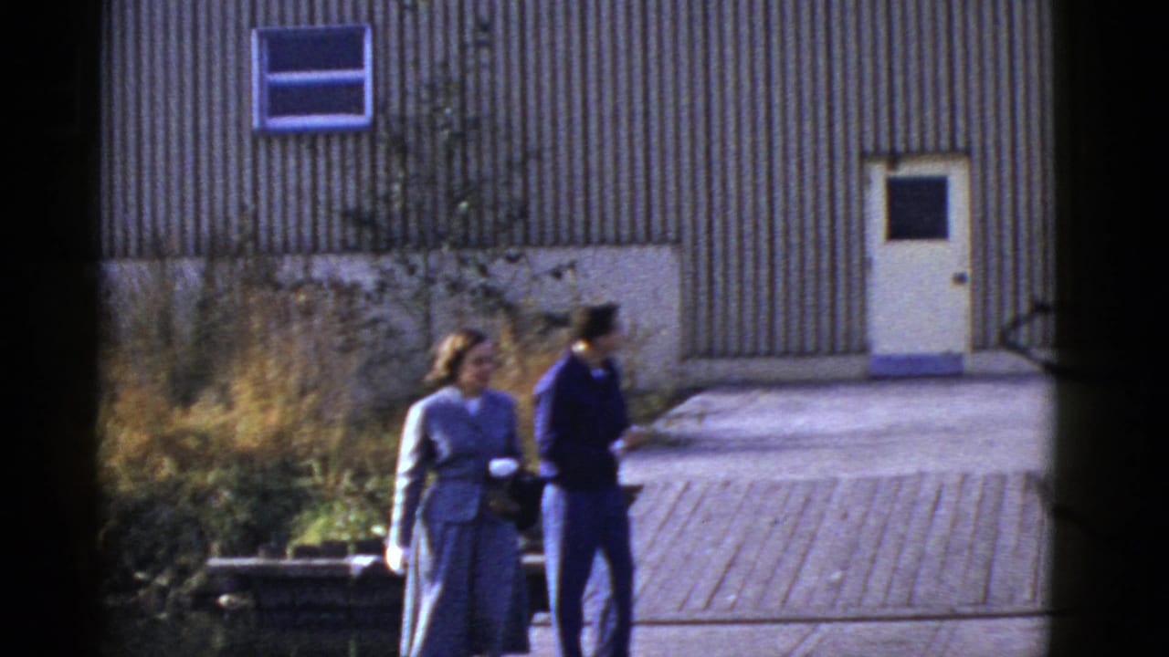 Couple walking together beside weeds and a corrugated building with a white door.