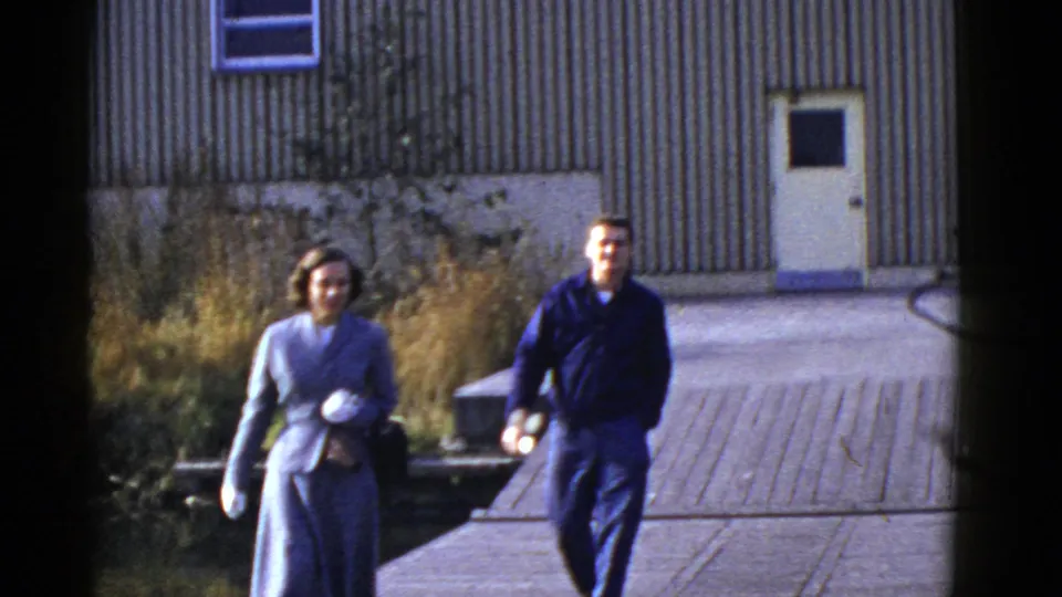 A woman in a light suit and a man in dark clothing walk toward the camera in a brief San Francisco 8mm home-movie moment.