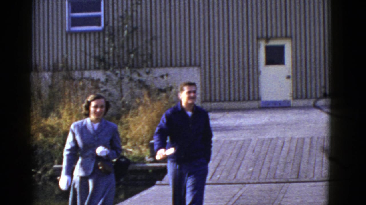 Early 1950s San Francisco home-movie frame showing a smiling man and woman walking from a corrugated building.