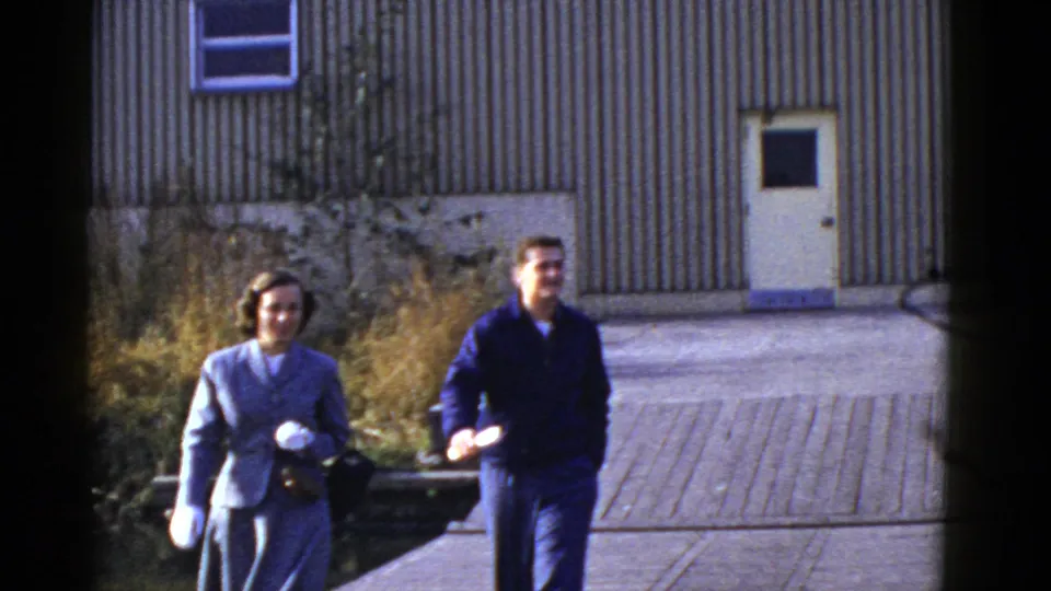 Early 1950s San Francisco home-movie frame showing a smiling man and woman walking from a corrugated building.