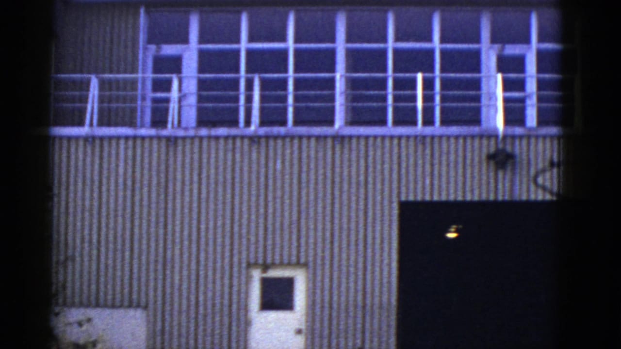 Upper windowed balcony above corrugated siding, with a white door and dark opening below.
