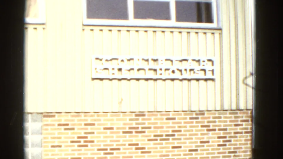 1950s San Francisco building facade with light siding, a window, brick base, and a partially legible exterior sign.