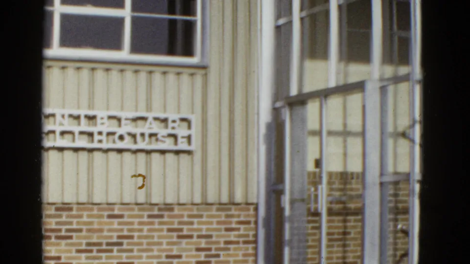 1950s San Francisco exterior view with wall lettering, beige siding, brickwork, and a metal-framed glass entrance.