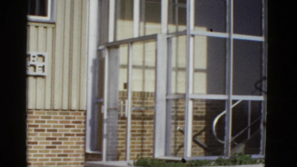 Home-movie frame of a metal-framed glass entrance, brick foundation, and partial building sign in San Francisco metadata context.
