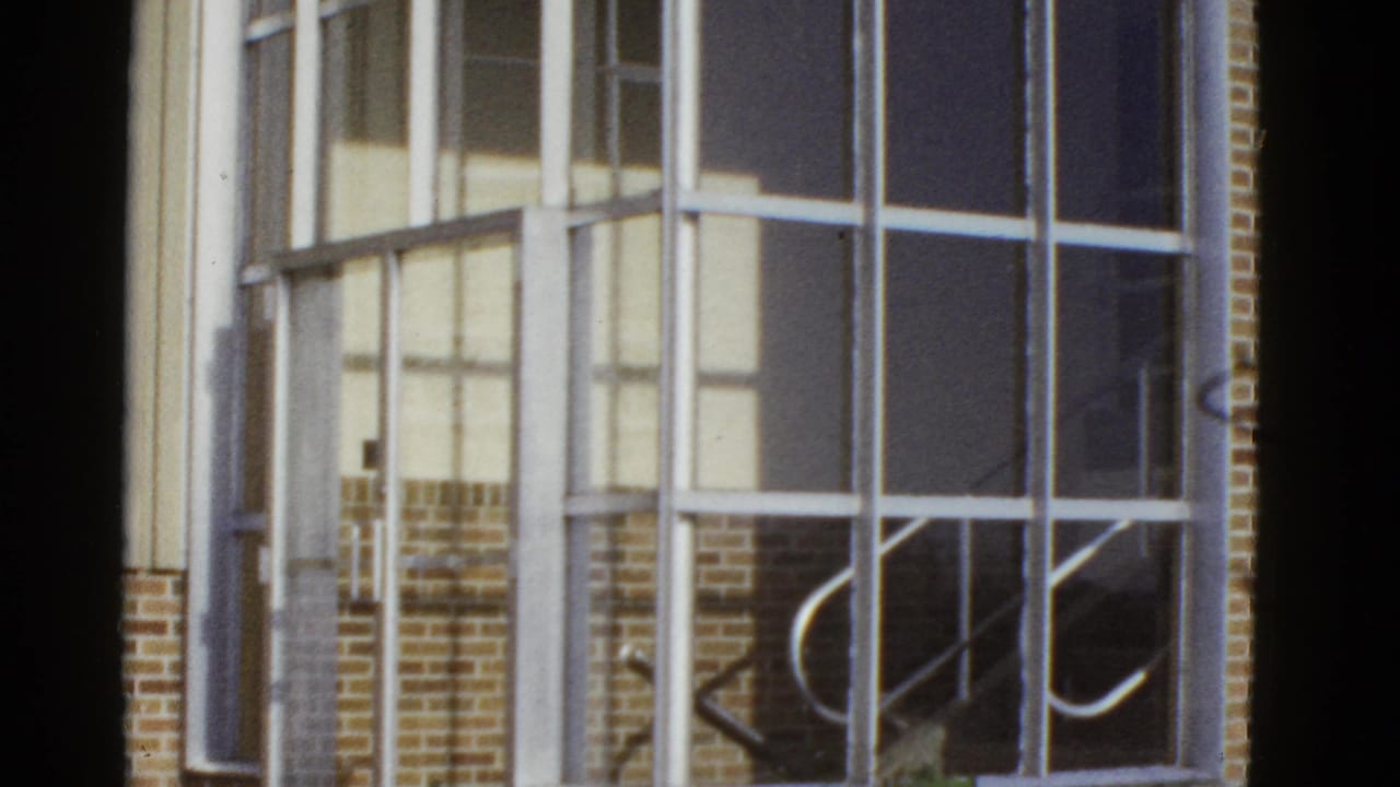 1950s San Francisco home-movie frame looking toward large window grids, brick facade, and reflected interior or stair details.