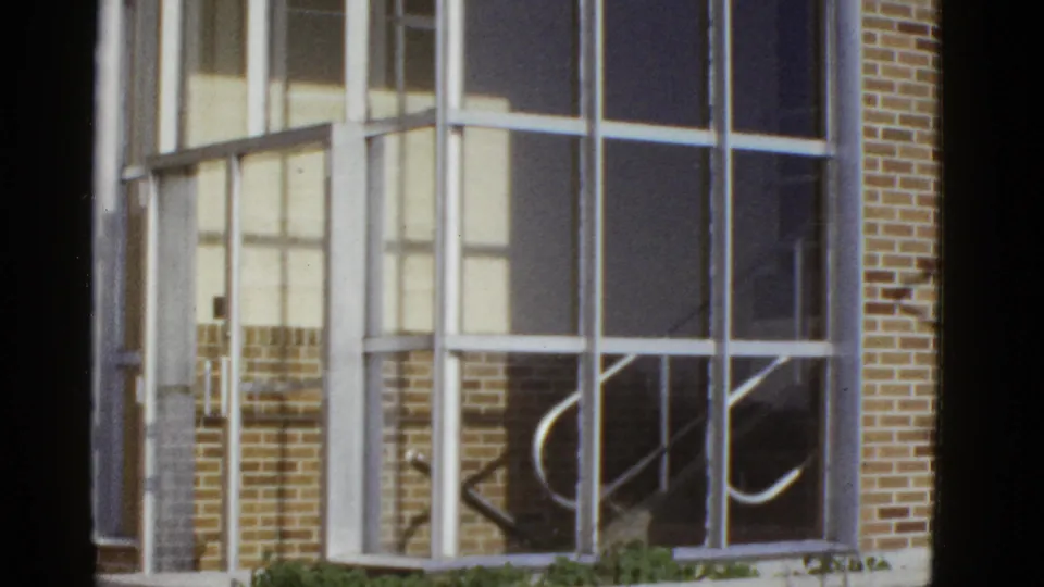 1950s San Francisco frame showing a large gridded window, brick exterior, pale wall panels, and curved stair rail reflections.