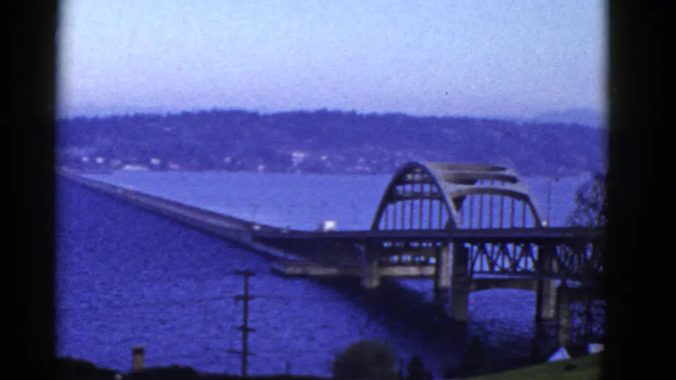 End frame of the 8mm bridge view, with the arched span at right, blue water below, and hazy hills beyond.