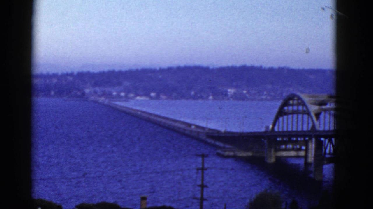 Bridge and arched span over water, with shoreline and wooded hills in the distance.