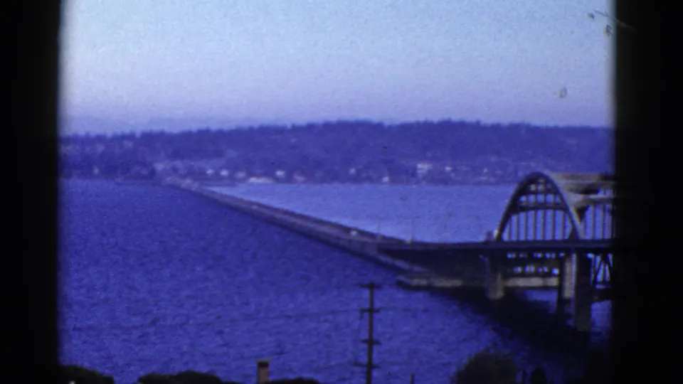San Francisco-area bridge panorama on 8mm film, showing blue water, an arched span, distant shore, and soft mid-century color.