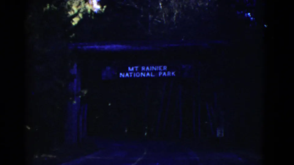 Blue-shifted 8mm frame of a dark entrance area with a visible MT RAINIER NATIONAL PARK sign above the roadway.