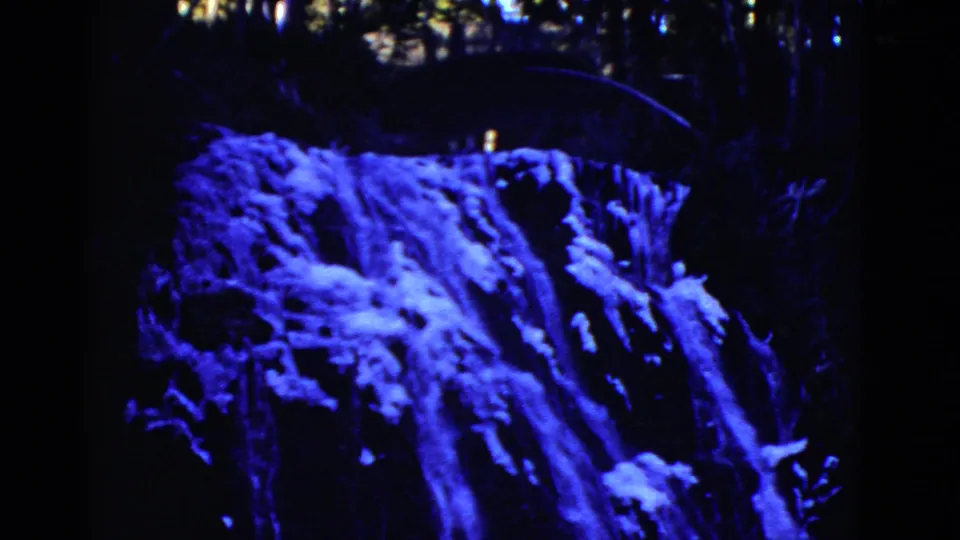 Early 1950s 8mm frame of a frozen waterfall or ice-covered rock face, rendered in strong blue color shift and deep shadow.