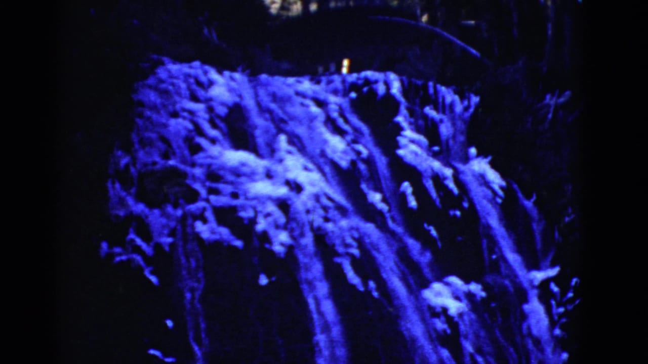 Blue-lit waterfall dropping over dark rocks with shadowed foliage around it.
