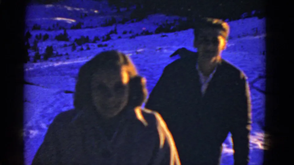 Two adults in winter coats walk through a snowy, blue-tinted landscape in 1952 San Francisco-linked home-movie footage.