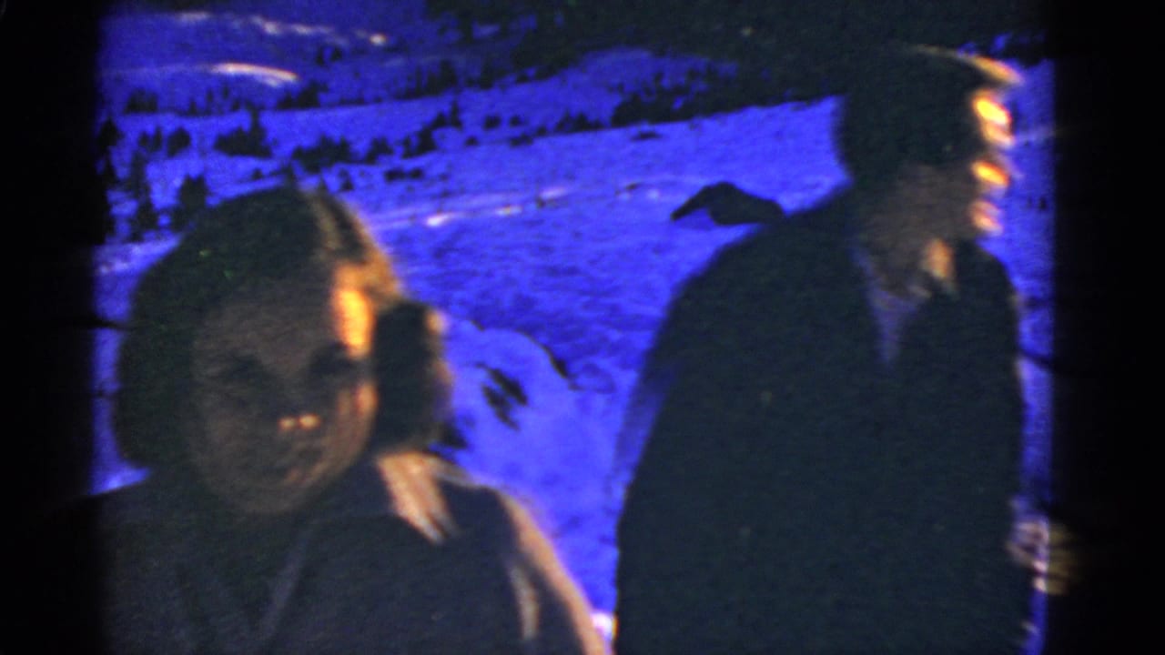 Early-1950s 8mm frame of a couple in winter clothing in a snowy mountain landscape, with a strong blue color cast.