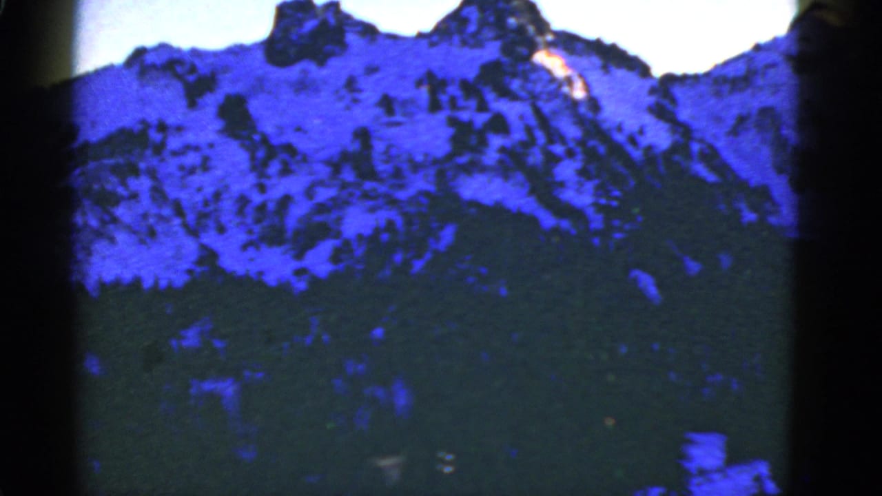 Snowy mountain ridge and forest seen through dark vertical film-frame edges.