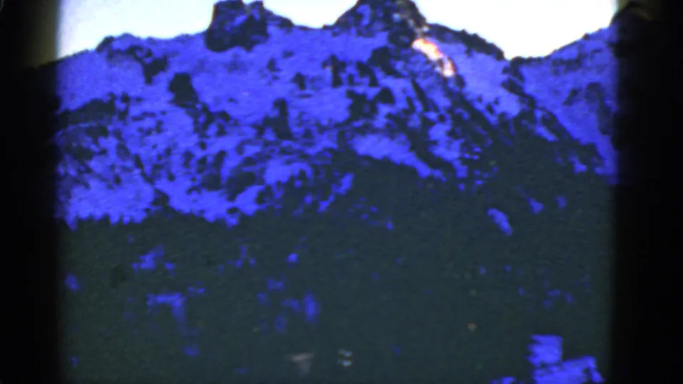 Blue-shifted 8mm view of a snow-covered ridge over dense forest, with dark gate edges and soft archival focus.