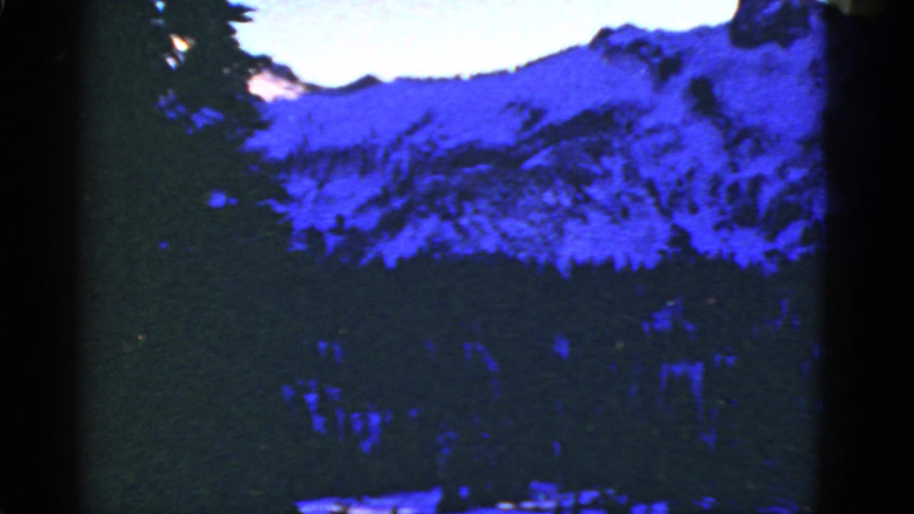 Blue-shadowed snowy mountain ridge and evergreen treeline in archival 8mm home-movie footage cataloged to 1952.
