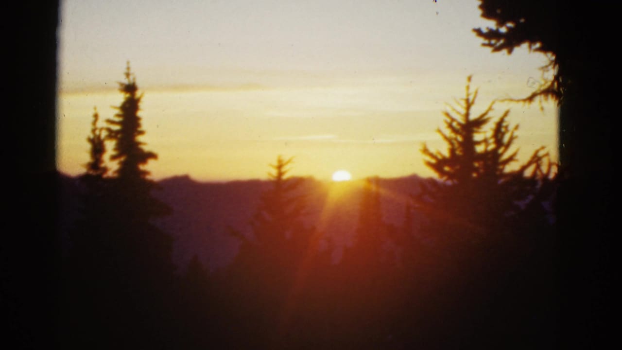 1950s color 8mm frame of a yellow sun near the horizon, silhouetted evergreens, and distant mountain ridges, location listed as San Francisco area.