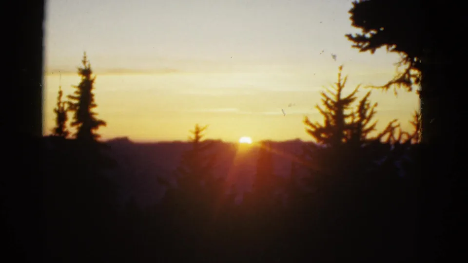 Final 8mm frame of the sunset, with the sun low over distant ridges and evergreen silhouettes against a warm sky.