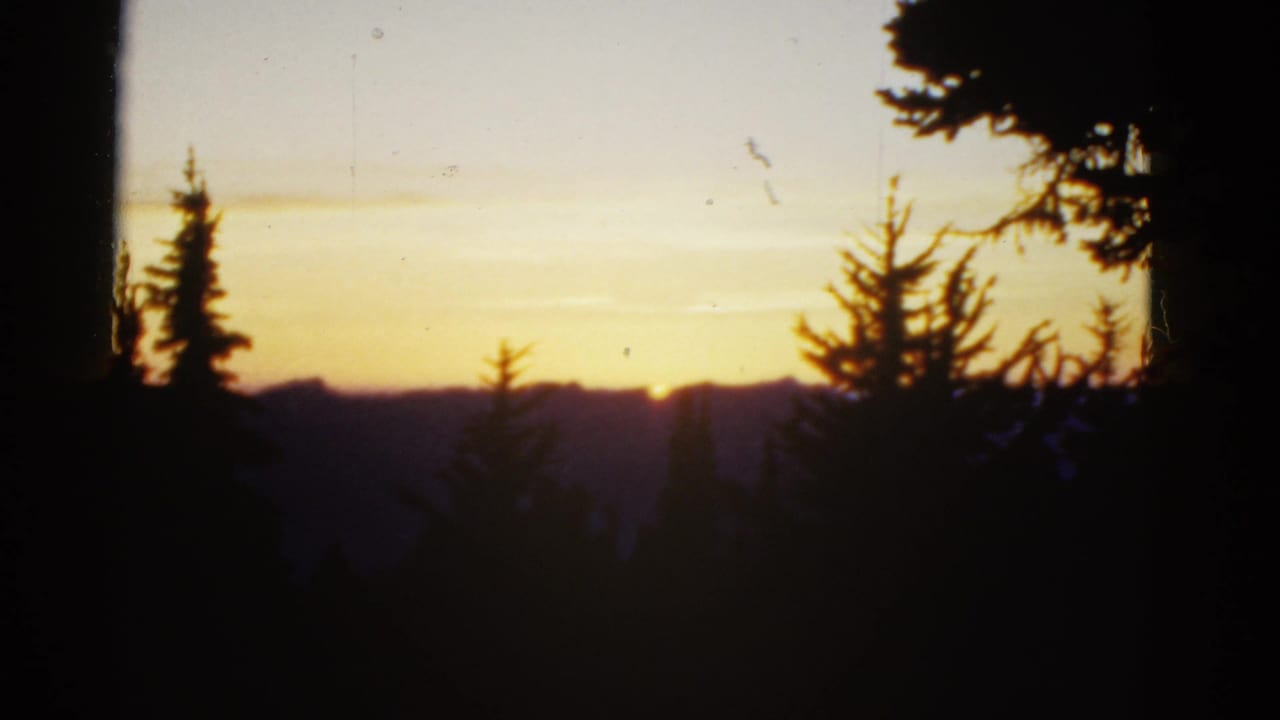 Sunset behind dark evergreen silhouettes and distant ridges.