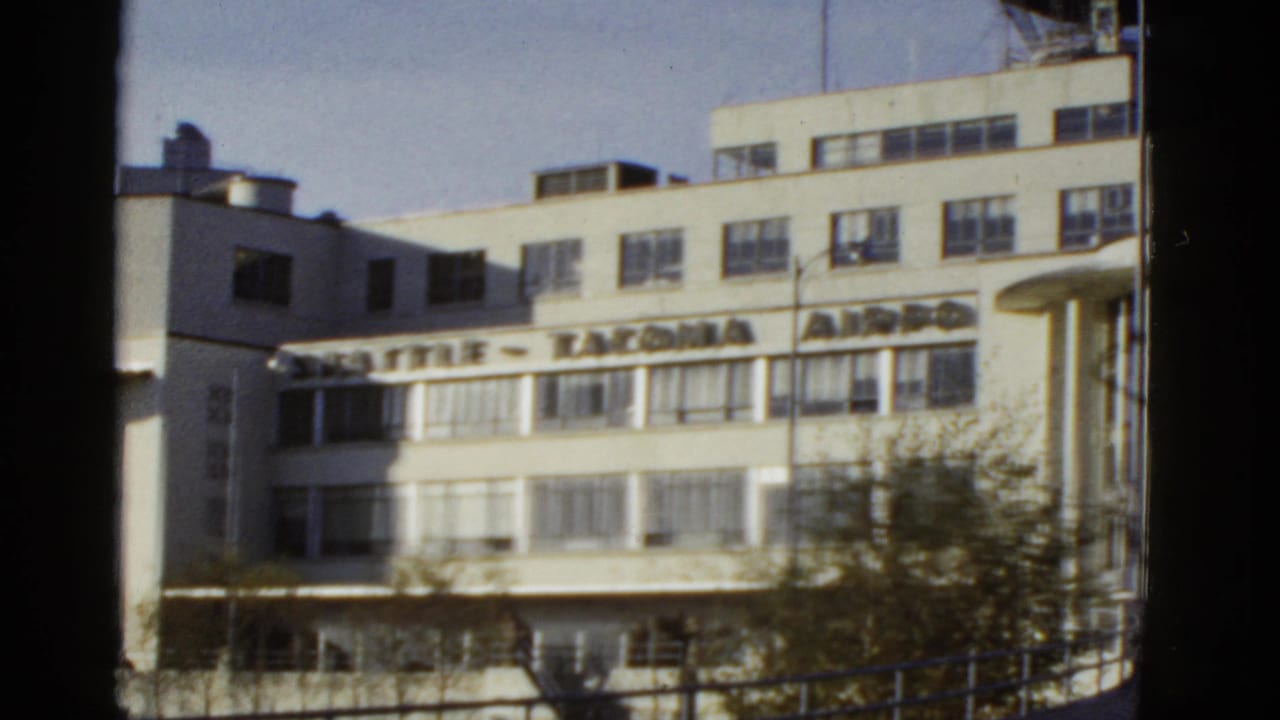 Reported 1950s airport terminal exterior, with prominent lettering across the facade and dark frame edges from the filming position.