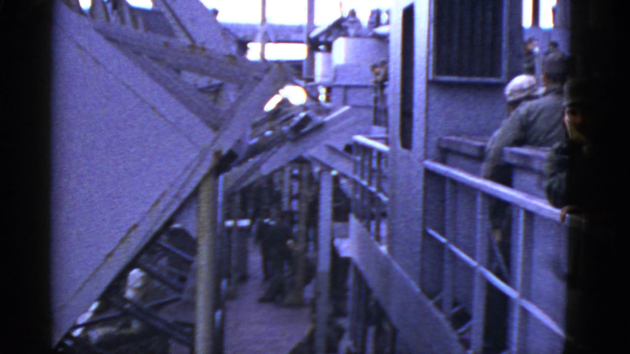 Early-1950s home-movie frame of uniformed men on a vessel deck, with railings, metal structures, and bright sky visible.