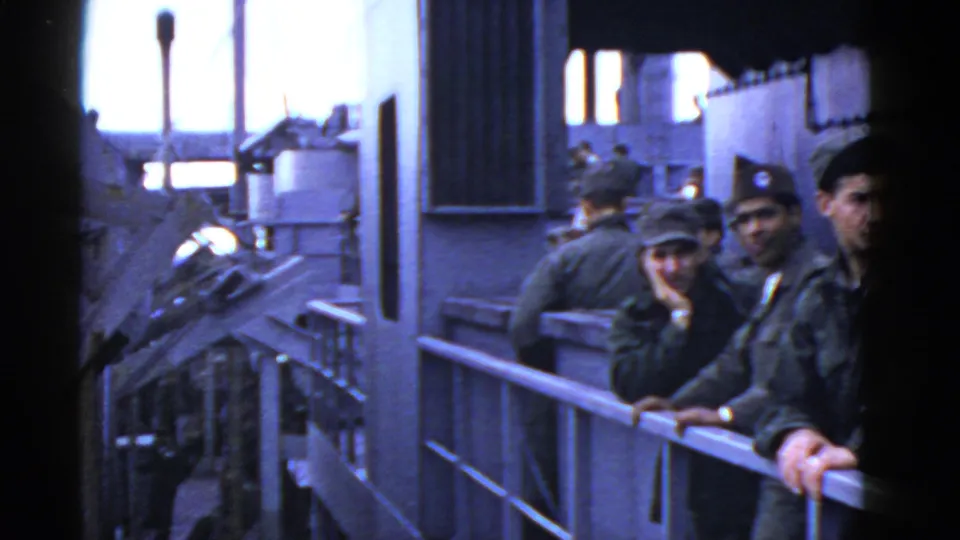 A small group of uniformed men, some in caps, stand close to the camera along a ship railing in archival 8mm footage.