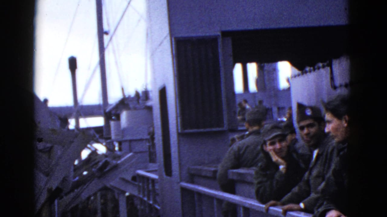 Early-1950s home-movie frame of sailors on a naval ship deck near San Francisco metadata context, with railing, ship structures, and ocean visible.