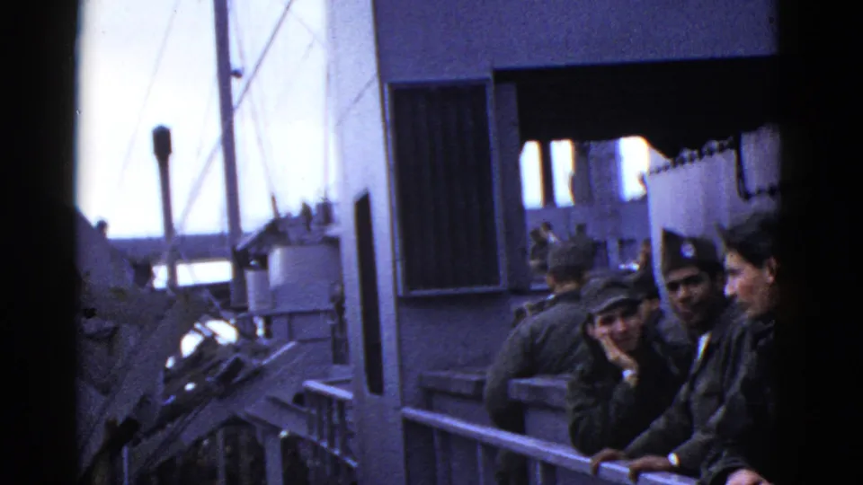 Early-1950s home-movie frame of sailors on a naval ship deck near San Francisco metadata context, with railing, ship structures, and ocean visible.