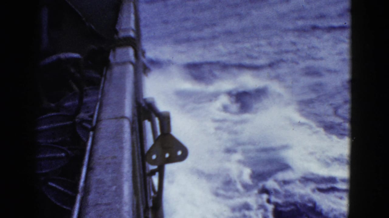 8mm frame from the ship's side, showing railing, dark deck equipment, and white wake moving through open water.