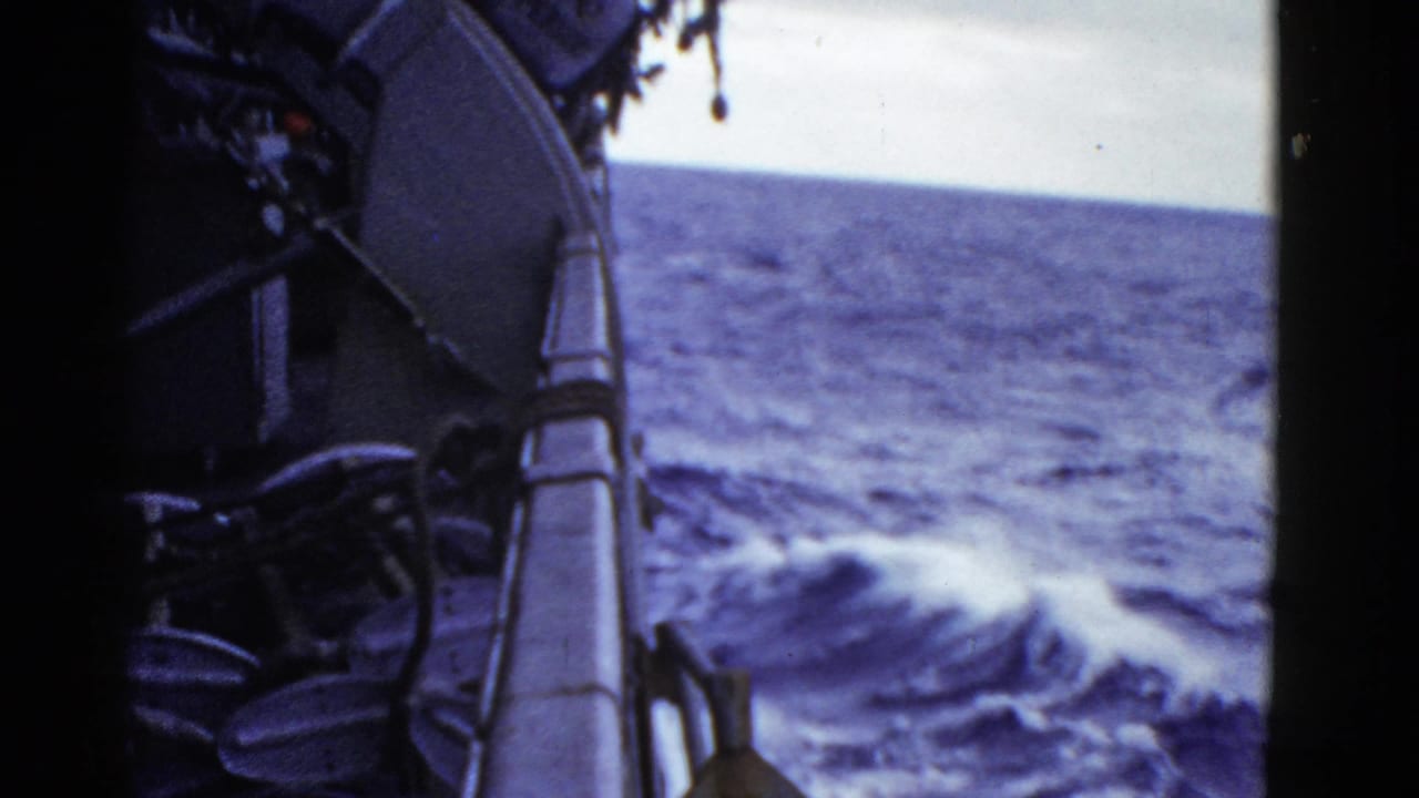 1952 8mm frame showing the side of a moving ship with rail, dark deck details, open water, and white wake.
