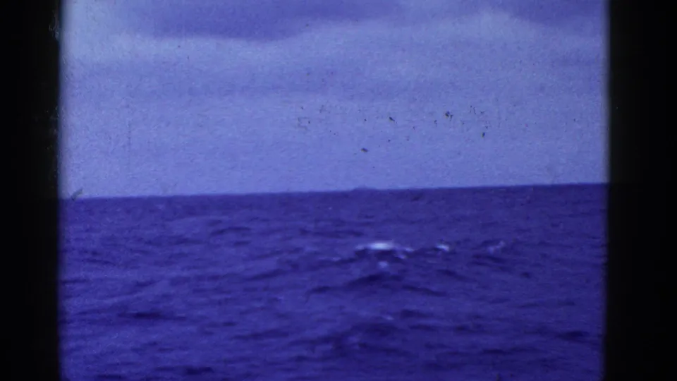 Metadata-supported 1950s home-movie view of open ocean near San Francisco, with low cloud cover, soft focus, film grain, and a dark frame edge at the left.