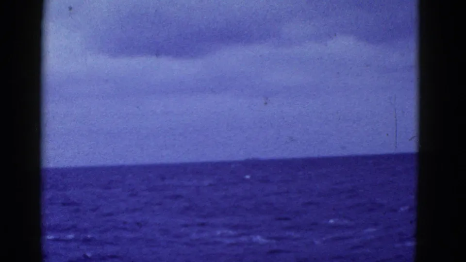 Metadata-supported 1950s 8mm frame of a cloudy ocean view near San Francisco, showing a tilted horizon, dark side borders, grain, and scratches.