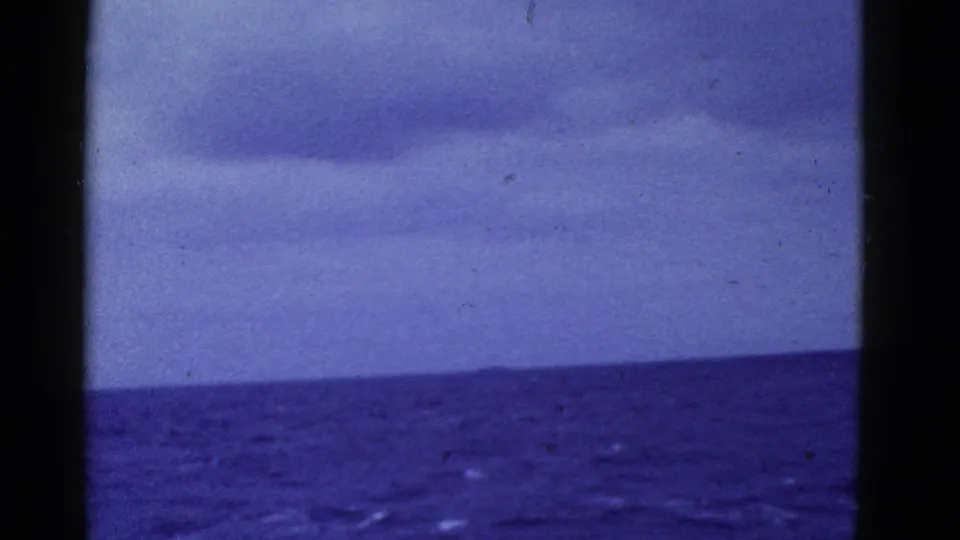 Metadata-supported 1950s home-movie frame showing dark blue ocean and low clouds near San Francisco, bordered by black film edges and a central dark divider.