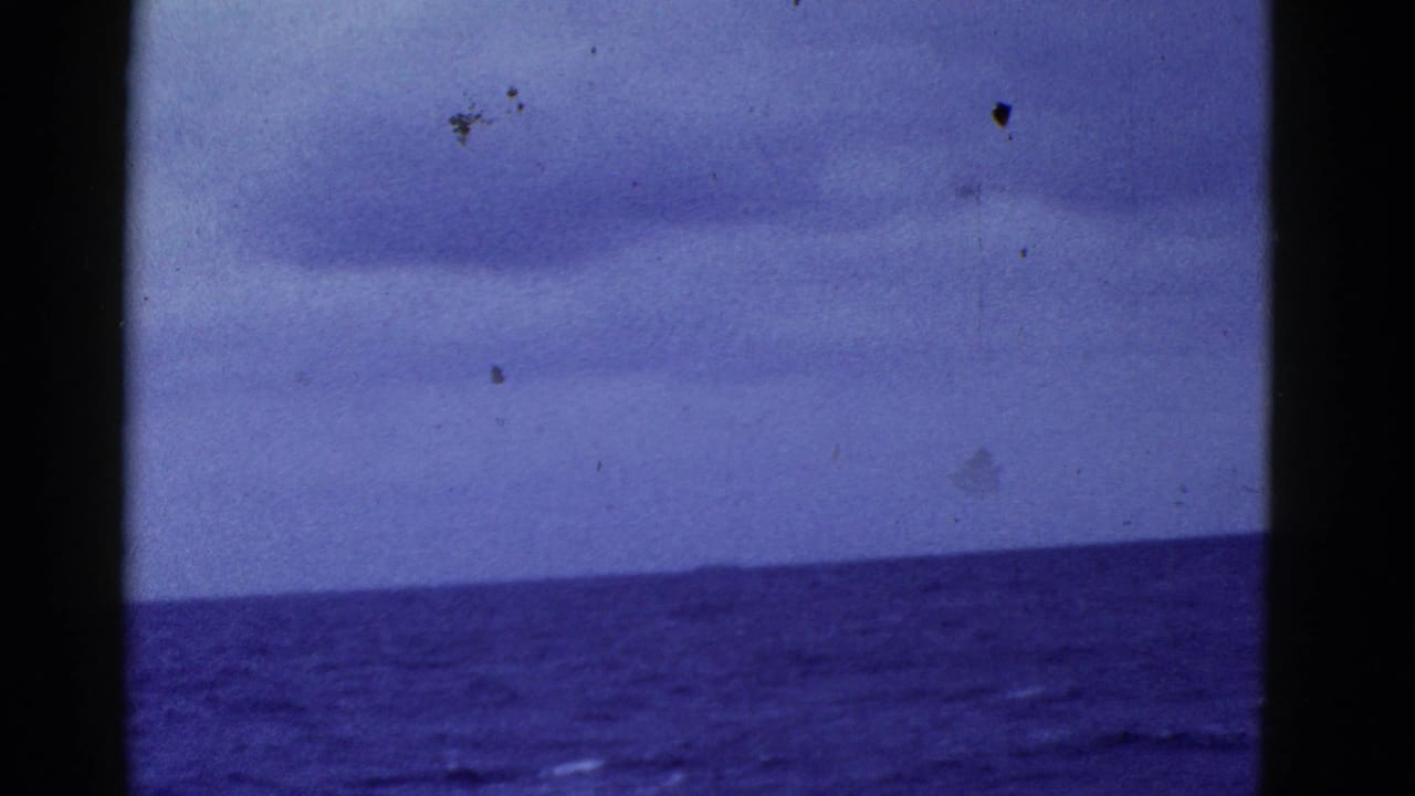 Open ocean beneath a cloudy sky with a distant horizon and dark film-frame borders.
