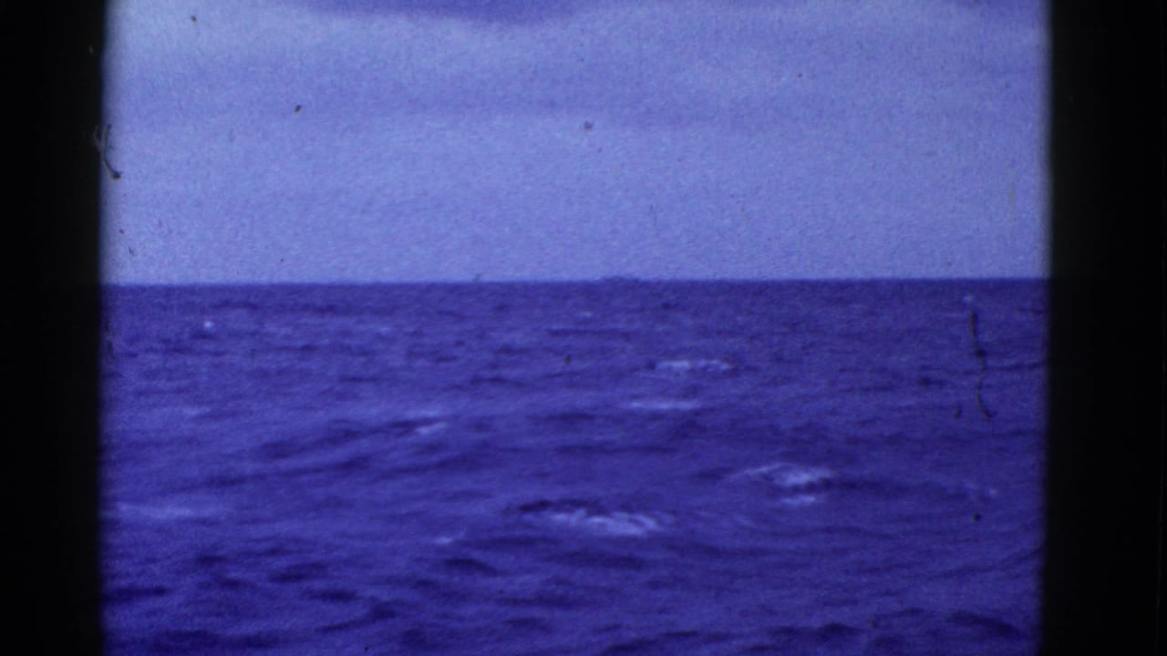1950s 8mm home-movie frame showing a blue open-ocean horizon under a pale sky, with film border and dust visible.
