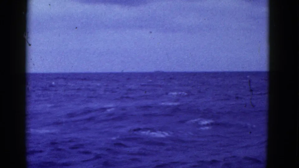 1950s 8mm home-movie frame showing a blue open-ocean horizon under a pale sky, with film border and dust visible.