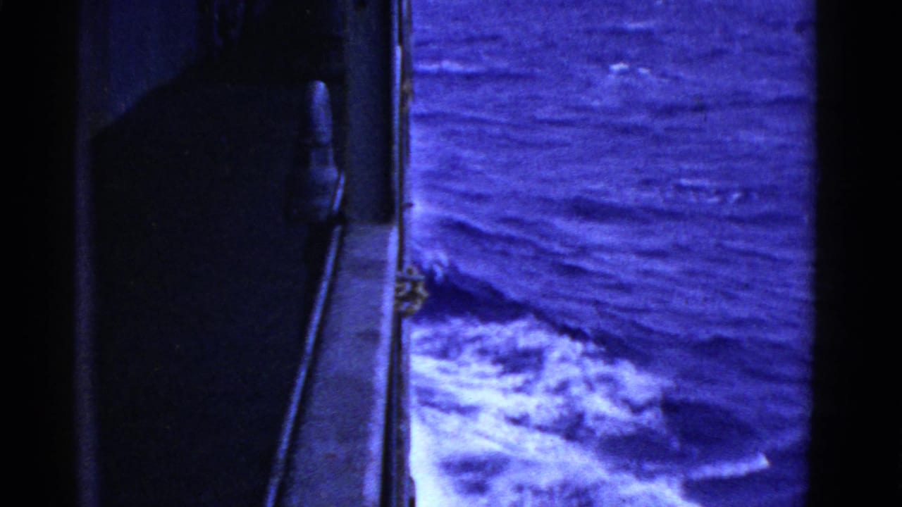 Side of a ship beside dark blue choppy water and white wake.