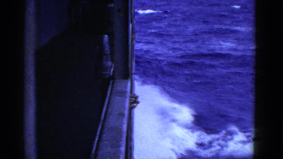 Early 1950s 8mm view from a ship side, with dark deck framing and white spray against blue ocean water.
