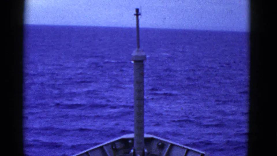 Ship bow and a central mast or post point toward an open blue ocean horizon in early 1950s 8mm footage.