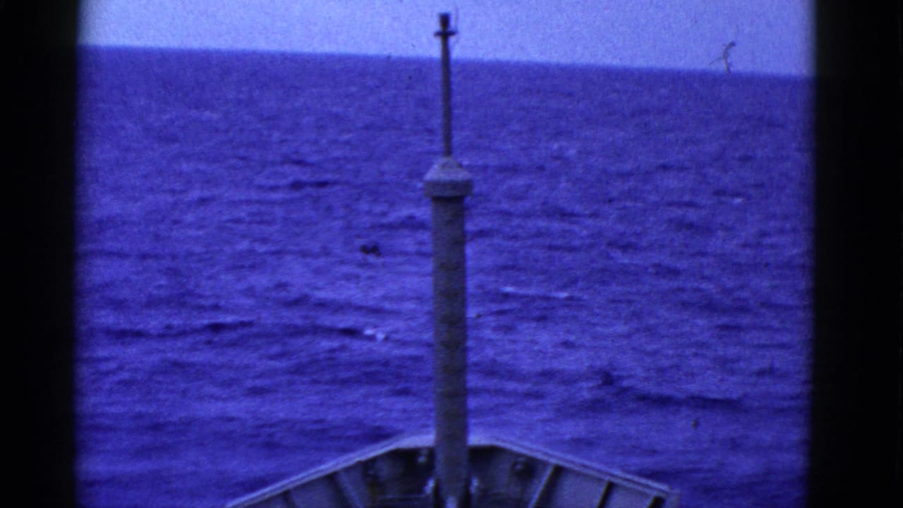 Ship bow and central mast seen ahead over blue open ocean.