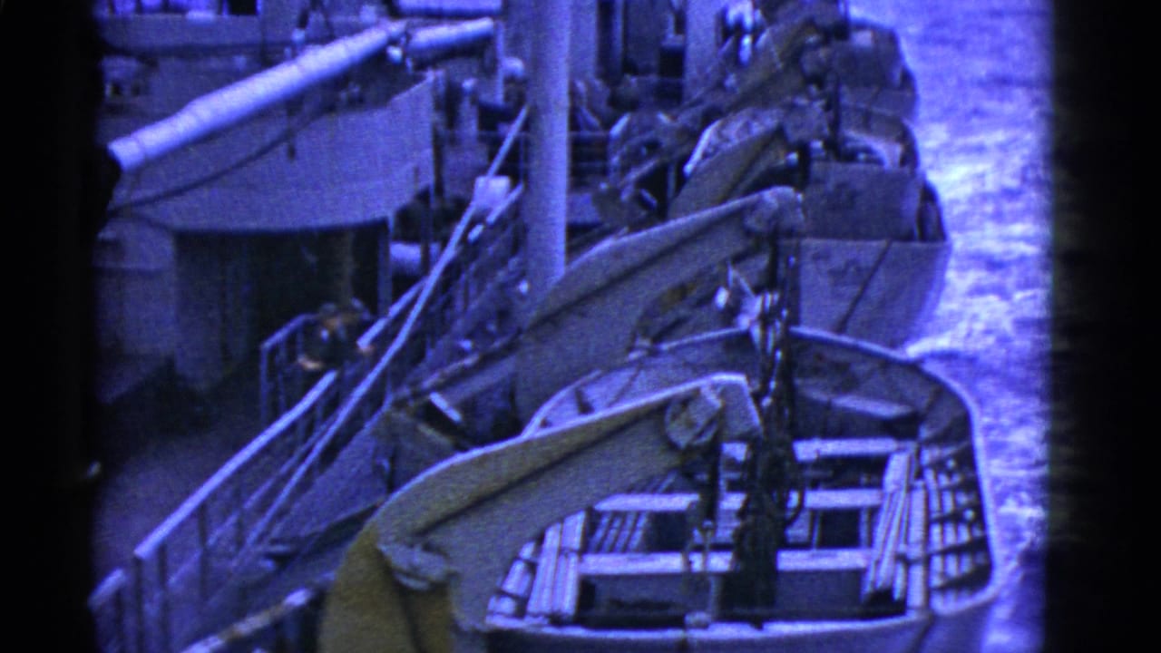 1950s San Francisco home-movie view of rowboats or lifeboats secured beside a large ship, with rigging and water visible.
