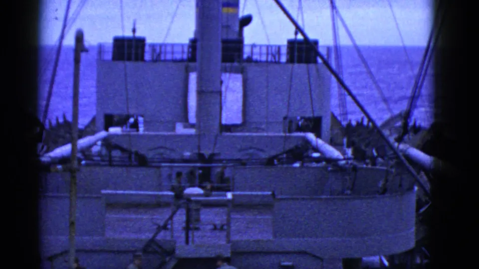 1950s San Francisco home-movie frame of a ship's deck structure, rigging, water, and distant people on or near the deck.