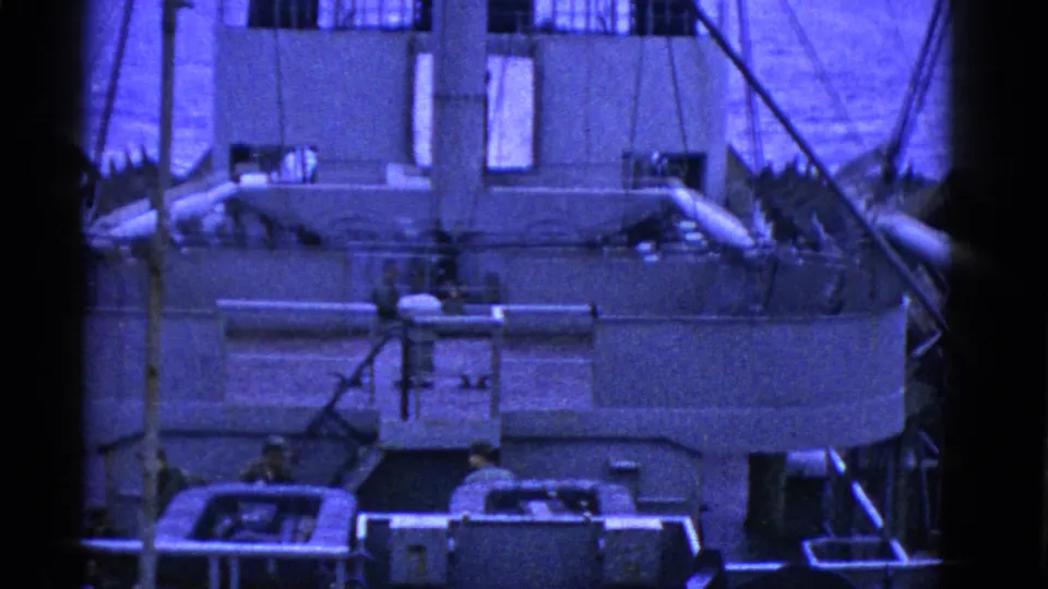 Blue-cast 1950s San Francisco footage shows the side of a large ship with rigging, railings, water, and distant deck figures.