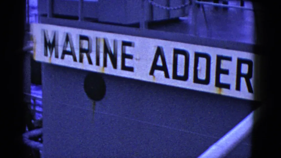 1950s 8mm close-up of the MARINE ADDER name painted on a ship hull, with dark metal plating and rust marks visible.
