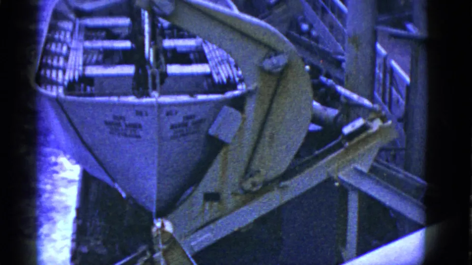 Early 1950s San Francisco frame with a small boat under or beside a crane arm, deck railings, pipes, and partially visible workers.