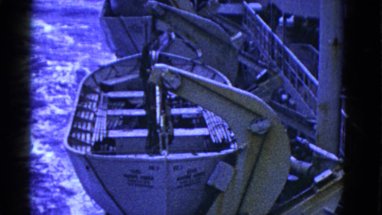 Lifeboat viewed from above with davit arm and water behind it.