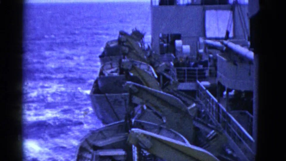 End-frame view of several lifeboats on davits along the ship side, with open water and deck structures visible.